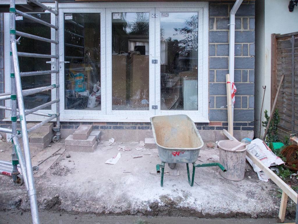 Unfinished rear extension works with a scaffold tower, wheelbarrow and rubble outside new patio doors