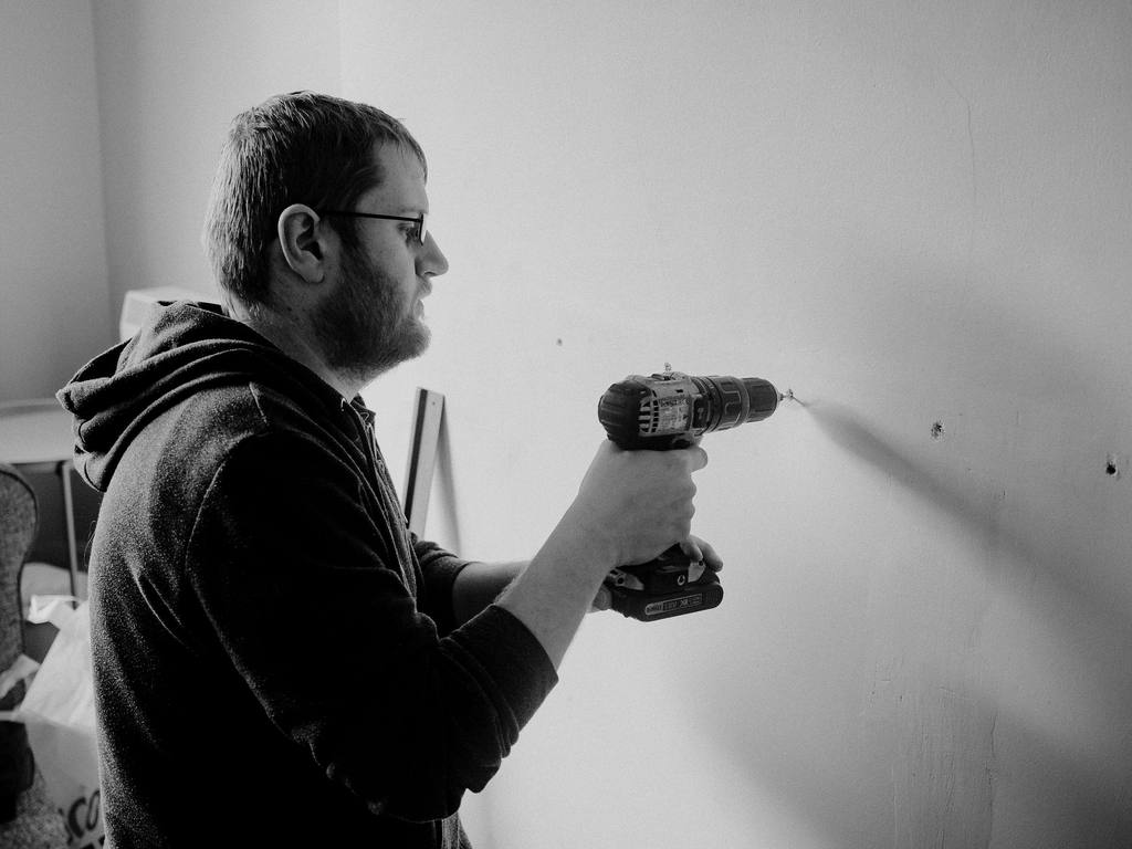 Tradesman using a power drill on an interior wall, in black and white
