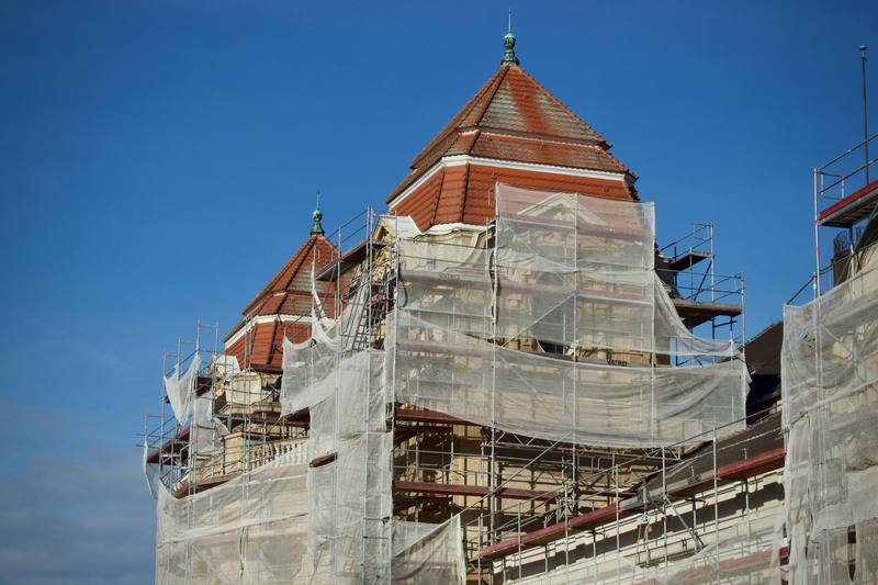 Red brick building under restoration, wrapped in scaffolding and protective netting