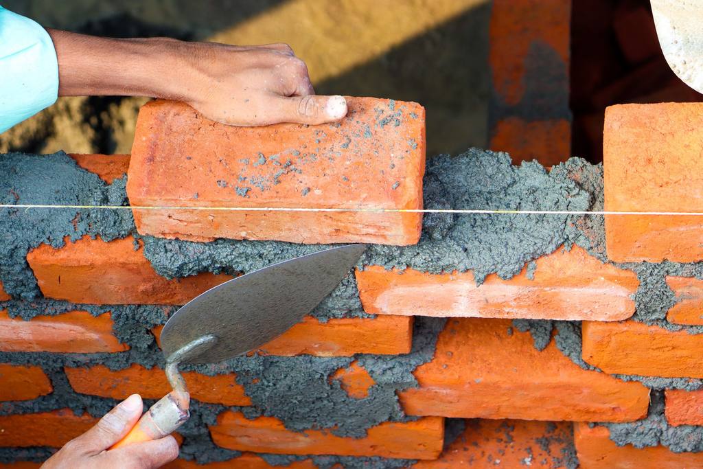 Bricklayer’s hands setting a red brick on fresh mortar with a trowel
